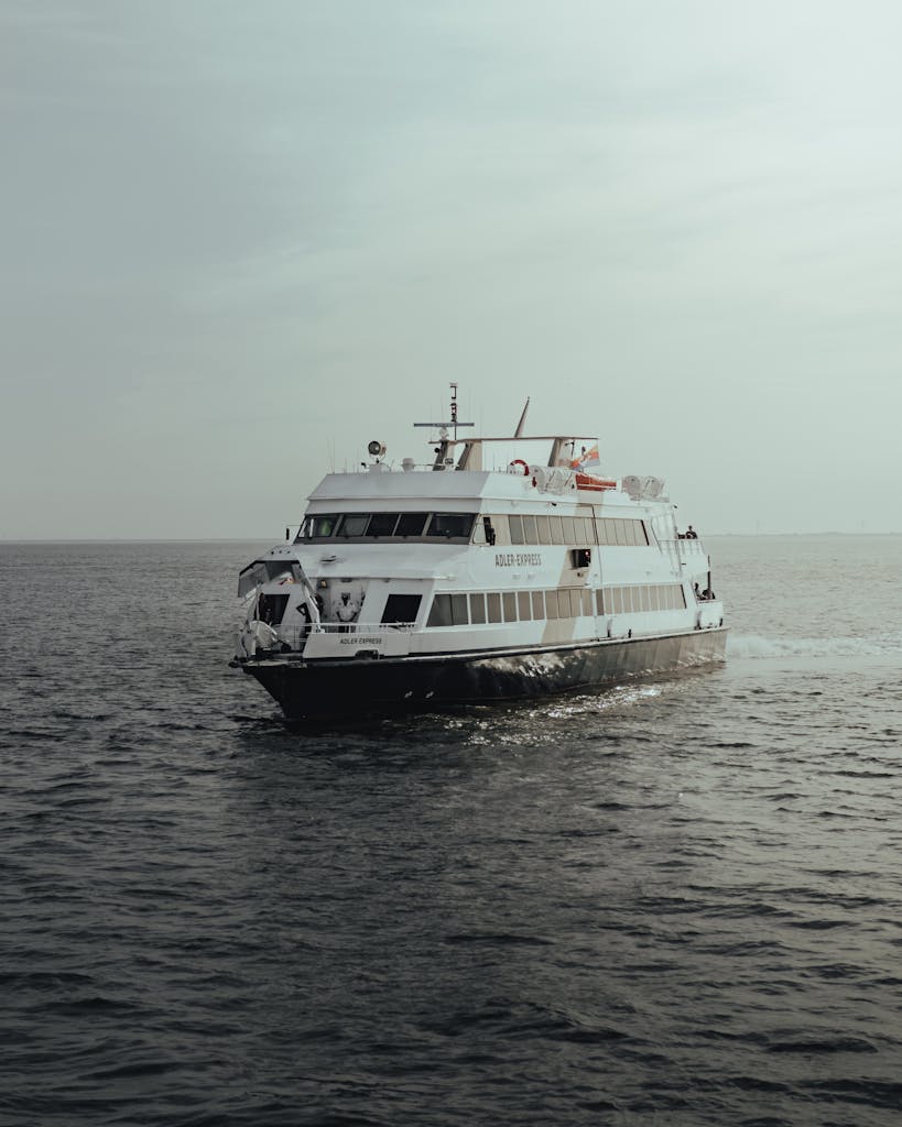 A modern passenger ferry cruising through calm open sea under a muted sky.